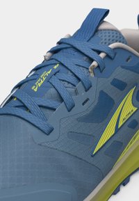 Μπλε αθλητικό παπούτσι με κίτρινο λογότυπο και λεπτομέρειες, με υφασμάτινη υφή, μπλε κορδόνια και ετικέτα που γράφει "ALTRA LONE PEAK 6".