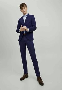 Marinblå kostym med slim-fit kavaj och matchande byxor, kombinerad med en ljusblå skjorta. Bruna läderskor fulländar outfiten.
