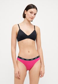 Top en lingerie noir avec des fines bretelles, associé à un slip rose avec une bande noire étiquetée "HUGO". Tissu lisse, design minimaliste.