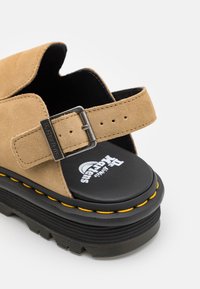 Sandal in suede tan con cinturino regolabile, suola platform nera e cucitura gialla lungo il bordo. Presenta una soletta con marchio.