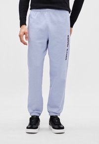 Ανοιχτό μωβ φόρμες με ελαστι�κή μέση, γαζωμένα μπατζάκια και τυπωμένο μαύρο λογότυπο στο πλάι. Συνδυασμένα με μαύρα αθλητικά παπούτσια.