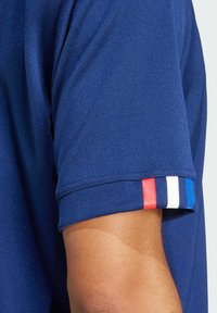 Mørkeblå sports polo-shirt med korte ærmer, der har en stribet accent i rød, hvid og blå på ærmet. lavet af tekstureret stof.