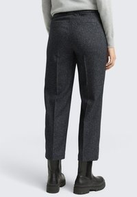 Hoge taille, donkergrijze broek gemaakt van gestructureerde stof, met taps toelopende benen en een plooi aan de voorkant. Gecombineerd met zwarte enkellaarsjes.