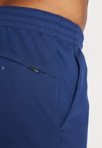 Marineblaue Sportshorts aus glattem Stoff, mit einer Reißverschlusstasche und einem elastischen Bund mit genähten Details.