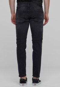 Sötétszürke, slim-fit farmernadrág sima textúrával. Hátul zsebekkel és lánc kiegészítő részlettel a derékpánton.