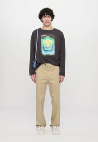 Donkergrijze lange mouwen shirt met kleurrijke ster-graphic, gecombineerd met beige broek en witte sneakers. Accessoire: lichtblauwe tas.