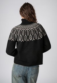 Schwarzer Strickpullover mit hohem Kragen und einem kontrastierenden gemusterten Einsatz in Creme und Grau, ausgestattet mit einem strukturierten Stoff und einem gerippten Saum.