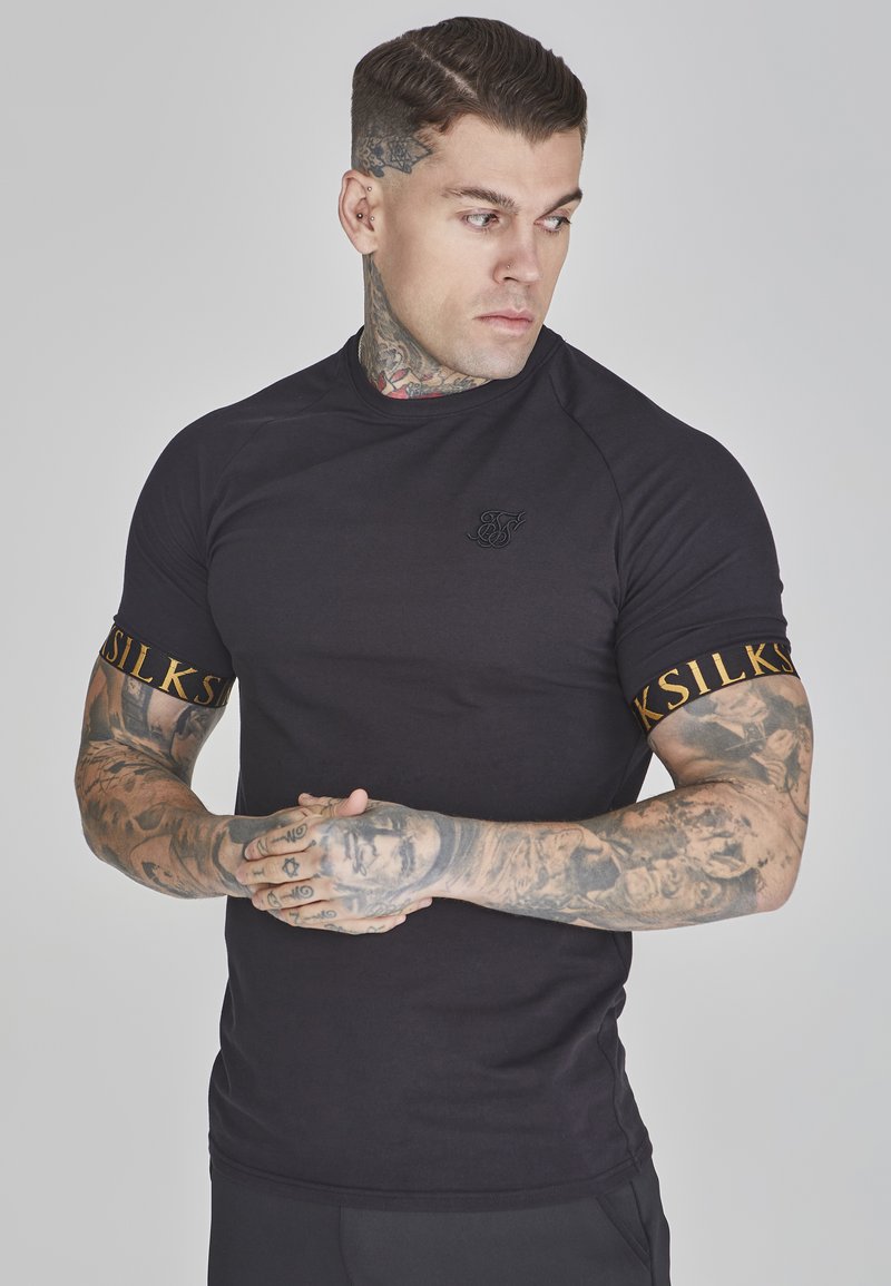 Zwart aansluitend T-shirt met korte mouwen en ronde hals, voorzien van een gouden accentlogo op de linkerarm en een gladde, rekbare stof.