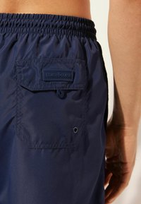 Marinum simbyxor med elastisk midja, bakficka med lock och logotyppatch. Lättviktig tygkvalitet, slät textur och minimalistisk design.