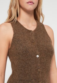 Brązowy wełniany bezrękawnik z okrągłym dekoltem, czterema guzikami z przodu i miękkim, teksturowanym wykończeniem.