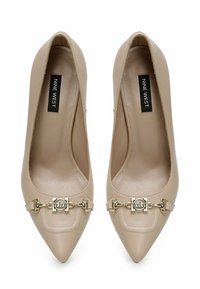 Beiga pumps med spetsig tå i slät konstläder, en dekorativ guldkedja vid tån och vadderade innersulor. Varumärkesetikett synlig.