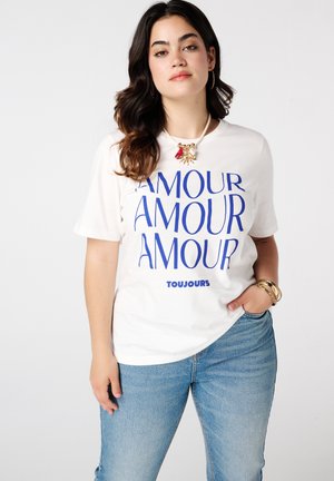 Witte katoenen t-shirt met grote blauwe tekst "AMOUR" die meerdere keren herhaald wordt en het woord "TOUJOURS" onderaan. Casual pasvorm, korte mouwen.