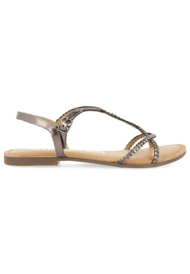 Sandalias planas en tono metálico bronce, con correas trenzadas, hebilla ajustable en el tobillo y una plantilla suave en beige con un diseño de suela mínimamente texturizado.