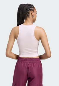 Svetloružový rebrovaný top s priliehavým strihom, skombinovaný s bordovými nohavicami na gumu v páse. Viditeľný vrkoč a kruhové náušnice.