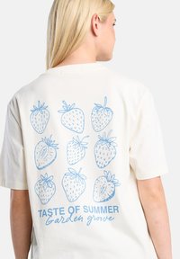 Cream-colored t-shirt featuring a light blue graphic of nine strawberries and text "TASTE OF SUMMER Garden grove" on the back. Short sleeves.