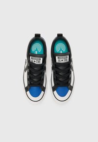 Črno-bela nizka športna obutev z modrim prednjim delom, črnimi vezalkami in turkizno notranjostjo. Na jeziku je znamka Converse All Star.
