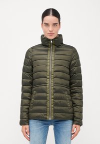 Veste rembourrée vert olive avec un col haut, fermeture éclair à l'avant, deux poches latérales et un motif matelassé horizontal. Texture lisse, conception légère.