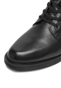 Czarna skórzana półbut z okrągłym noskiem, z zapięciem na sznurowadła, teksturowaną powierzchnią i mocną czarną gumową podeszwą.