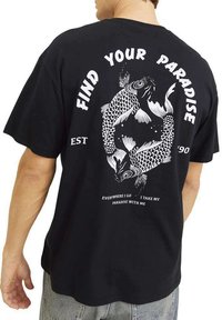 T-shirt nera con una grande grafica bianca di due pesci koi, testo che recita "TROVA IL TUO PARADISO" e ulteriori elementi testuali sotto.