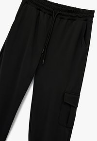 Schwarze Jogginghosen aus glattem Stoff, mit elastischem Bund und Kordelzug, Seitentaschen und einer Cargotasche am Bein.
