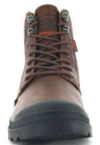 Zapatos marrones impermeables con un upper de cuero texturizado, suela de goma negra y ojales metálicos. Presenta cordones resistentes y un cuello acolchado.