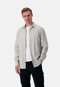 Camicia a righe con bottoni in verde chiaro e bianco, realizzata in tessuto morbido, con vestibilità rilassata, colletto e chiusura con bottoni. Abbinata a pantaloni neri.