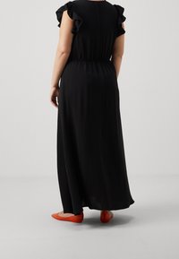 Svart maxiklänning med korta volangärmar, elastisk midja och avslappnad passform. Buren med klara orange platta skor, vilket ger en kontrast i färg.