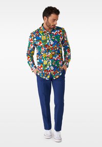 Buntes langärmliges Hemd mit verschiedenen Cartoon-Charaktergrafiken auf blauem Hintergrund. Kombiniert mit navyblauen Hosen und weißen Sneakern.