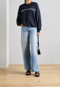 Granatowy sweter z nadrukiem "Marc O'Polo", jasnoniebieskie szerokie dżinsy oraz czarne sandały na platformie. W komplecie mała czarna torebka.