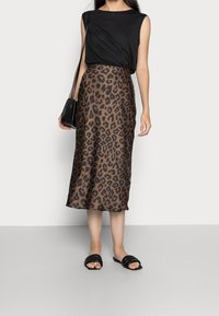 Top nero senza maniche abbinato a una gonna midi con stampa leopardata marrone. Il modello indossa sandali neri scivolati e porta una piccola borsa a tracolla nera.