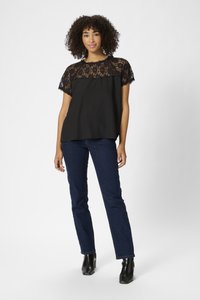 Black top with lace overlay at shoulders and neckline, paired with dark blue jeans and black ankle boots. Smooth fabric with textured lace detail.