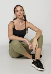 Top negro sin mangas, pantalones cortos color verde oliva y zapatillas negras con tachuelas. Modelo sentada, con un pañuelo de flores en la cabeza. Fondo neutro.