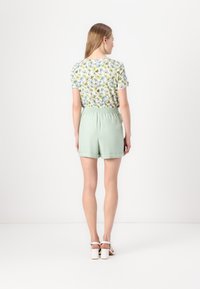 Calções verde claro com cintura elástica, combinados com uma blusa de manga curta com padrão florido apresentando tons de branco, azul e verde.