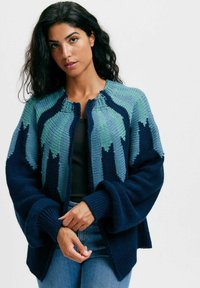 Stickad cardigan i blå och gröna nyanser, med ett texturerat mönster, öppen front och vida ärmar. Ribbad detalj vid ärmslut och nederkant.