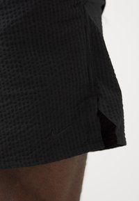 Pantalones cortos deportivos negros con una tela texturizada, que presentan un pequeño logo negro de Nike y aberturas laterales para facilitar el movimiento.