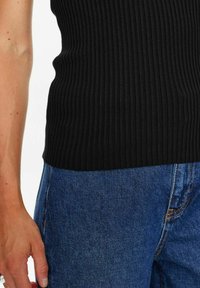 Černý žebrovaný tílko spárované s modrými džíny. Materiál je texturovaný a přiléhavý, s viditelným pasem a lehkými švy.