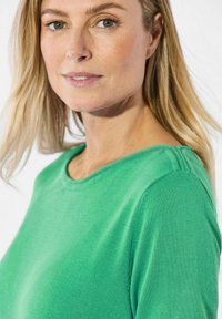 Groene gebreide trui met een ronde hals en geribbelde mouwen. Opvallend detail is een naadaccent op de schouder. Zachte textuur.