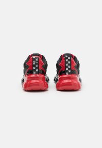 Schwarze und rote Sportschuhe mit gepolstertem Schuhkragen, gemusterten Schnürsenkeln und einer dicken, glänzenden roten Sohle. Enthält auffällige Logoakzente an der Rückseite.