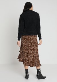 Svart fluffig tröja med långa ärmar, kombinerad med en leopardmönstrad, lager-på-lager midi-kjol med fransar och svarta ankelstövlar.