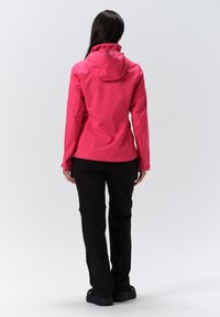Waterproof pink jacket with adjustable hood, fitted design, and long sleeves; paired with black pants and sturdy footwear.