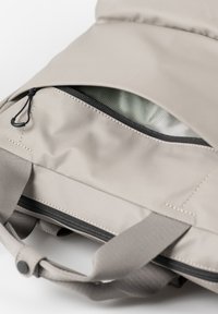 Beige stoffen tas met een ritsvak, voorzien van een gladde textuur en stikdetails aan de buitenkant. Het binnenvak heeft een lichtgroene voering.