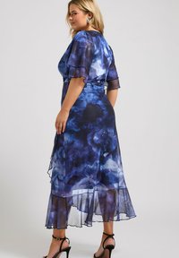 Blommig klänning i blåa och lila nyanser, genomskinligt tyg, korta fjäderlätta ärmar, lager av fåll och ankelsandaler.