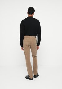 Pantaloni in velluto a coste marroni con un design a gamba dritta, abbinati a un maglione nero aderente. Texture liscia, dettagli minimi e tasche piatte.