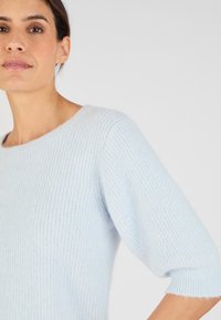 Maglione azzurro chiaro lavorato a maglia con scollatura rotonda, texture a coste e maniche corte. Materiale morbido e peloso con una vestibilità ampia.