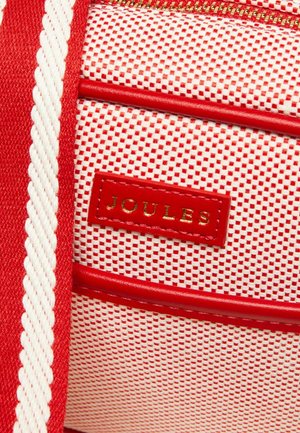 Rot-weißes strukturiertes Gewebe mit einem roten Lederlogo-Patch mit der Aufschrift "JOULES" und einem roten Reißverschlussdetail.