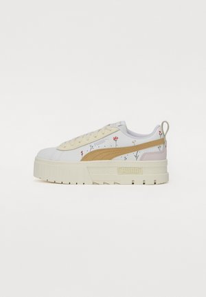Baskets blanches Puma avec semelle épaisse beige, bande beige, petits imprimés floraux et languette arrière, vues de profil extérieur.