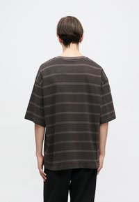 Camiseta de rayas grises con mangas cortas, que presenta un corte holgado y líneas horizontales texturizadas. Cuello simple y diseño minimalista. Vista posterior.