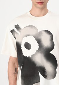 Krämfärgad t-shirt med en stor svart abstrakt blommönster med mjuka kanter, rund mitt och korta ärmar.