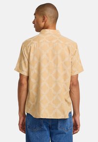 Short-sleeve, light yellow shirt made of soft fabric, featuring a large, cream geometric pattern with a relaxed fit and open collar.