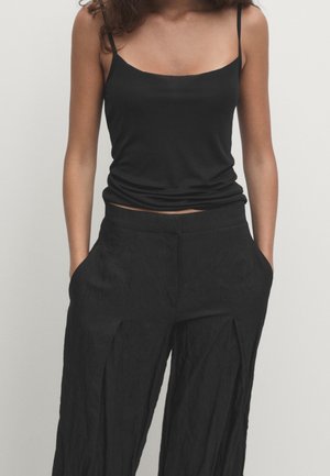 Czarny top na ramiączkach z cienkimi regulowanymi paskami, zestawiony z luźnymi czarnymi spodniami z przodu z zakładkami i bocznymi kieszeniami, wykonanymi z teksturowanej tkaniny.